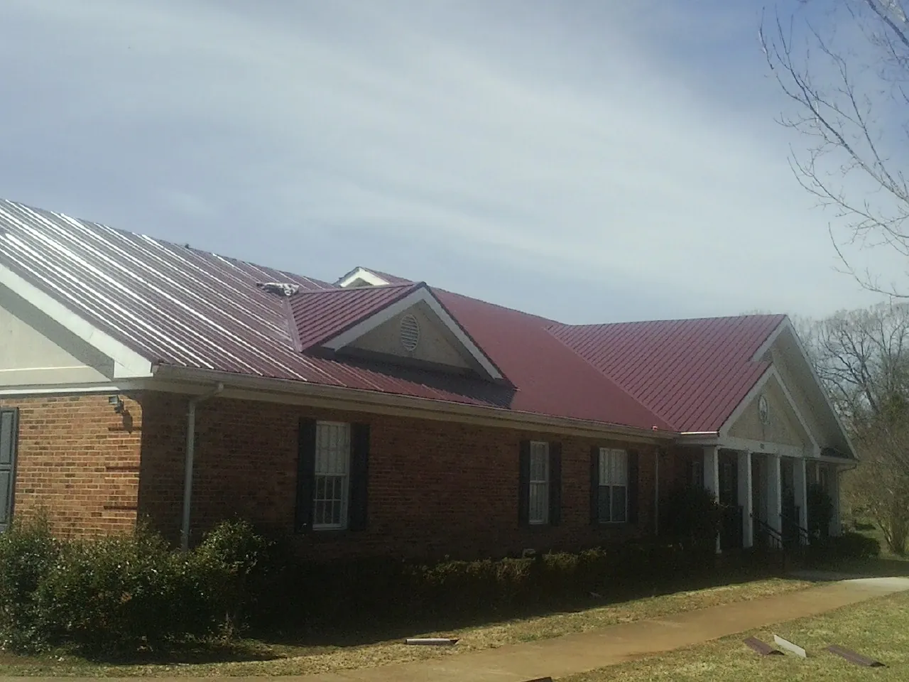 Red metal roof with gabled entries on a long brick building, from a Hail Damage Roof Repair job in San Marcos