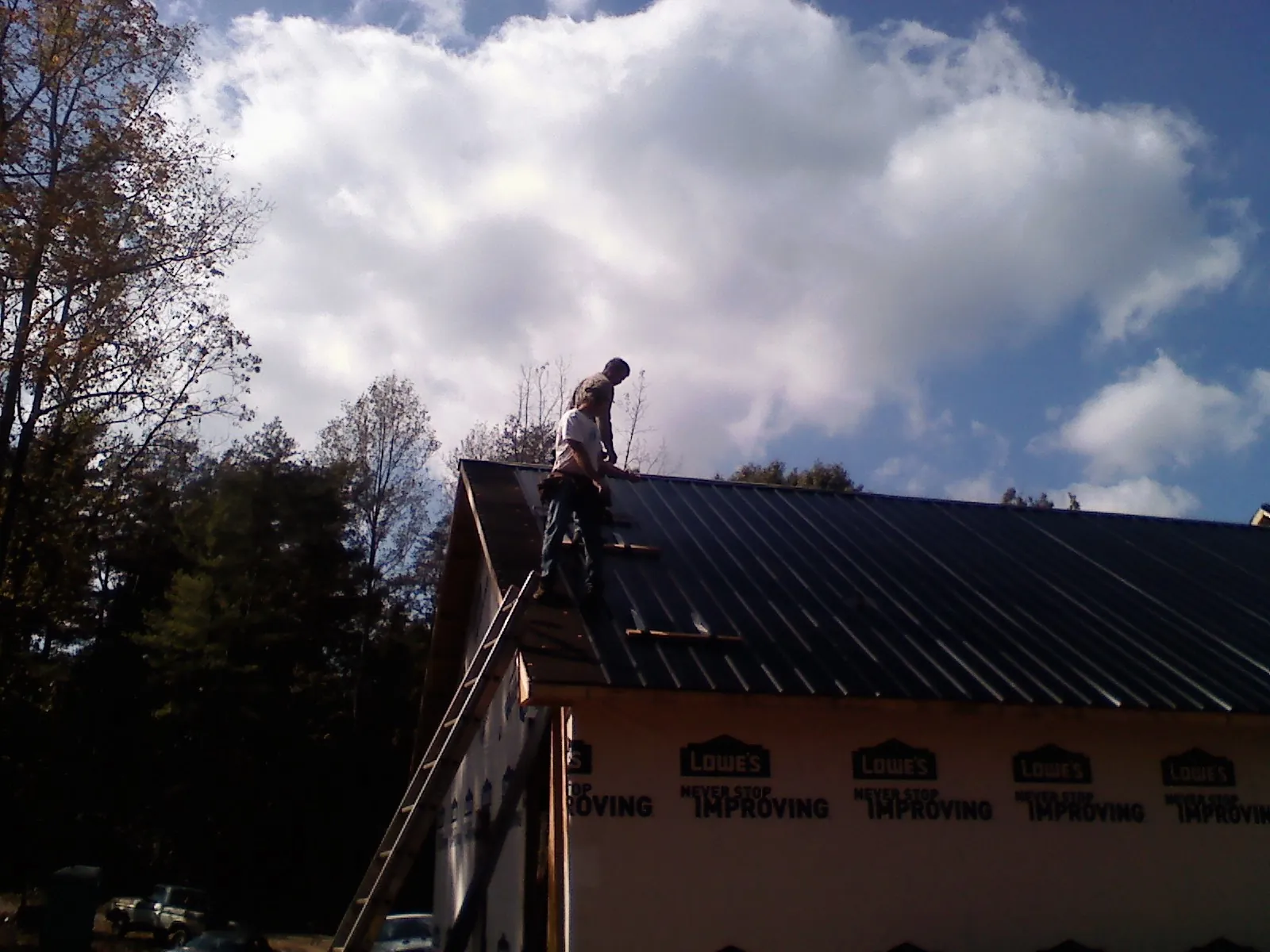 Roofer fastening dark metal panels high against a cloudy sky, from a Roof Inspection job in San Marcos