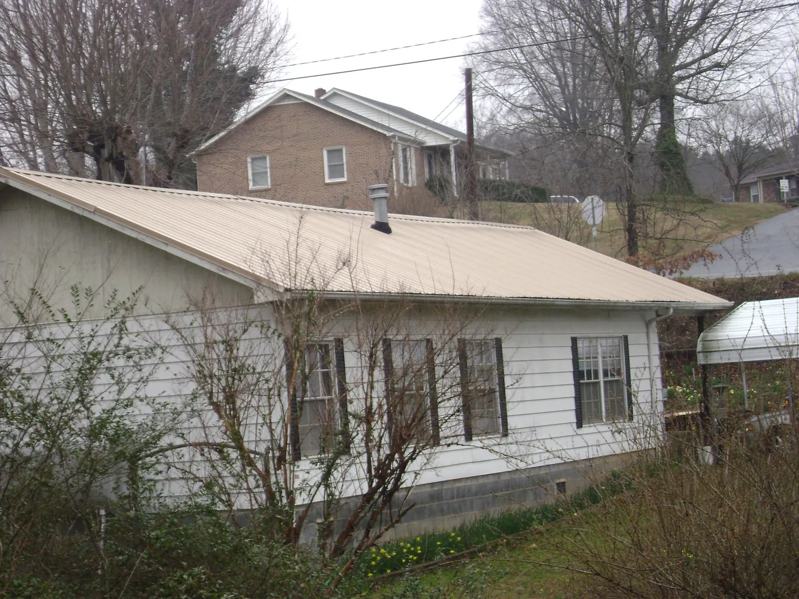 Tan metal roof on a white sided house set into a hillside — Commercial Roofing by Roofing Brothers in San Marcos