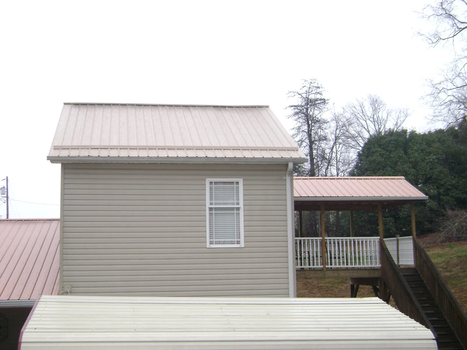 Tan metal roofs on a two story addition and attached porch, from a Roof Replacement job in San Marcos